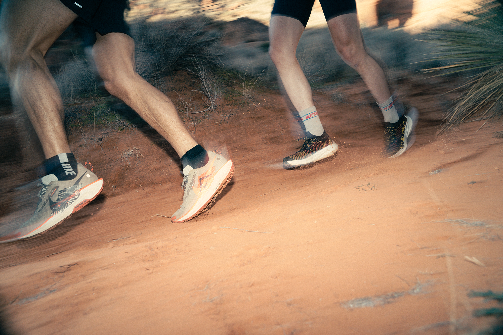 Two runners on a dirt path with a focus on their shoes and legs.